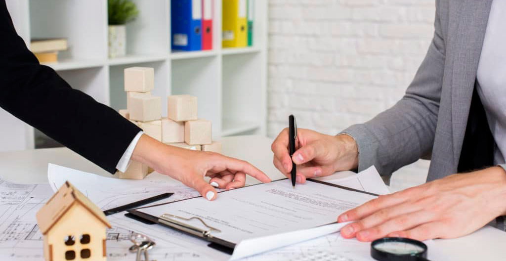 Mains tenant un document contractuel avec un stylo, sur un bureau légèrement encombré de dossiers